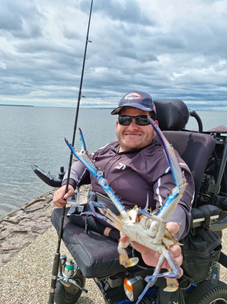 Adventure Image - Mark with a fishing rod in one hand, holding up a big blue swimmer crab in the other hand.