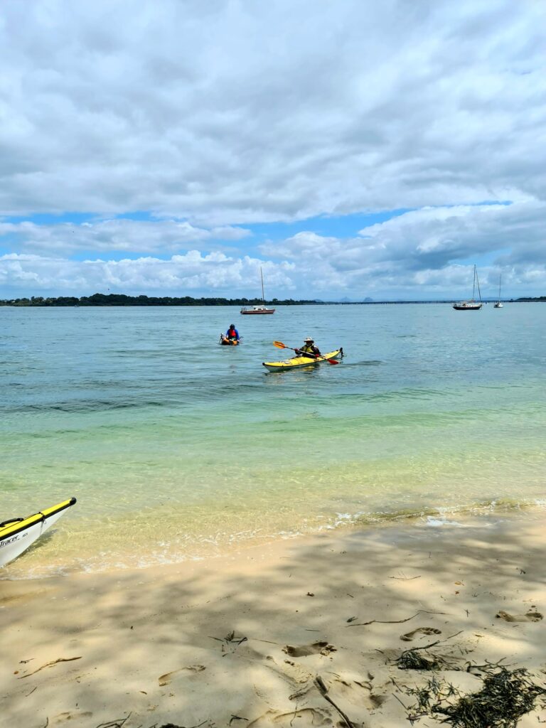 Adventure Image - Jim and Damien kayaking on beautiful blue green water just out from a sandy beach.
